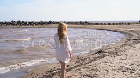 一个穿着白色裙子的金发女孩走在海岸线上视频的预览图