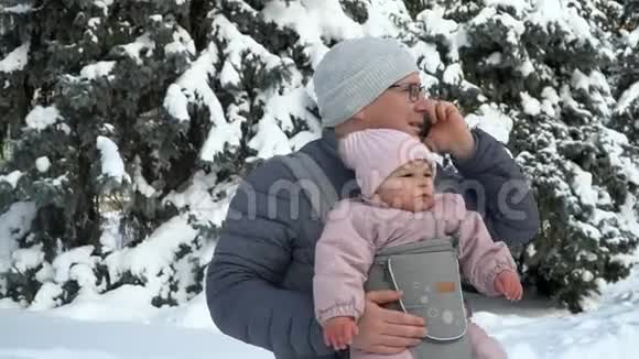 年轻的父亲抱着孩子带着讲电话的工作父亲视频的预览图