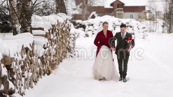年轻的新婚夫妇跑着在滑雪胜地的村庄里玩着玩手里拿着木头小屋靠近原木冬季视频的预览图