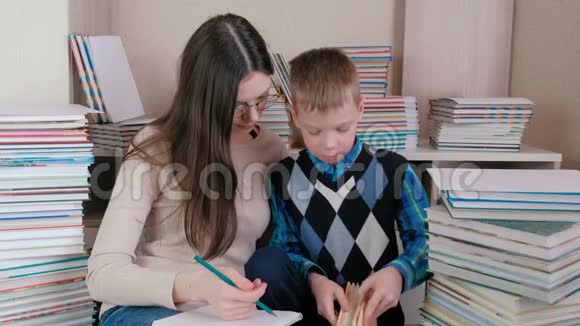 妈妈和儿子一起读一本书妈妈戴着眼镜在笔记本上写东西视频的预览图