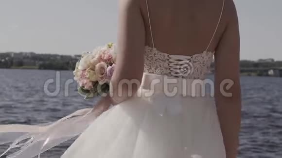 一个迷人的新娘的中倾手里拿着一个精致的婚纱站在湖边在远处眺望视频的预览图
