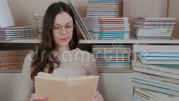 年轻的黑发女人戴着眼镜坐在中间大声读着一本书视频的预览图