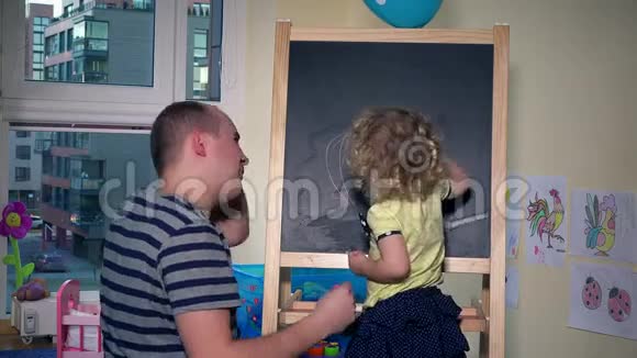 女孩用粉笔在黑板上画画父亲专心学习数字视频的预览图