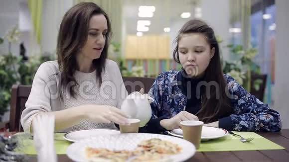 妈妈和女儿在咖啡馆里吃披萨和茶在披萨店吃晚饭快餐中不健康的食物视频的预览图