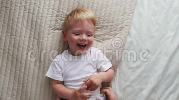 妈妈挠了挠躺在床上的男孩他直视着摄像机大声笑视频的预览图