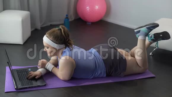 懒女孩在社交媒体上聊天躺在健身房垫子上而不是运动锻炼视频的预览图