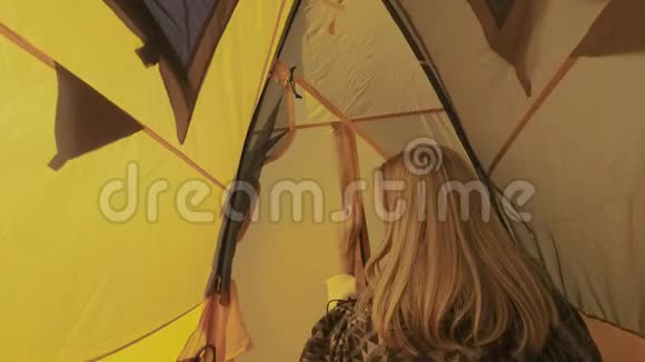 年轻女子打开帐篷入口女孩从帐篷里偷看出来在大自然中露营乡村之旅一种好奇视频的预览图