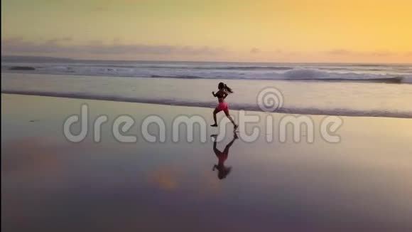 在日落海滩背光的跑步锻炼中用无人驾驶飞机对迷人的亚洲运动跑步女子进行空中淘洗视频的预览图