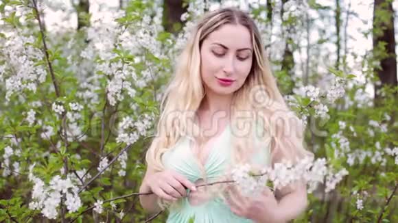 金发女人站在开花的灌木丛中视频的预览图