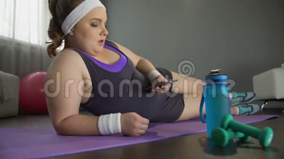 懒惰的肥胖女孩滚动她的手机而不是运动锻炼减肥视频的预览图