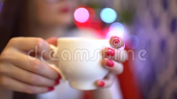 那个女人在咖啡馆里喝茶或咖啡那个女人坐在咖啡馆的一张小桌子旁手拿着一个杯子靠近视频的预览图