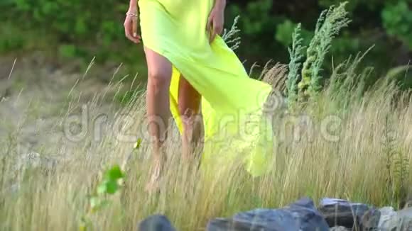 美丽的小女孩的双腿穿着黄色的长裙光着脚在沙滩上沙滩上散步海风习习视频的预览图