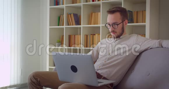 年轻英俊的白种人商人在笔记本电脑上打字看着镜头开心地坐着微笑视频的预览图