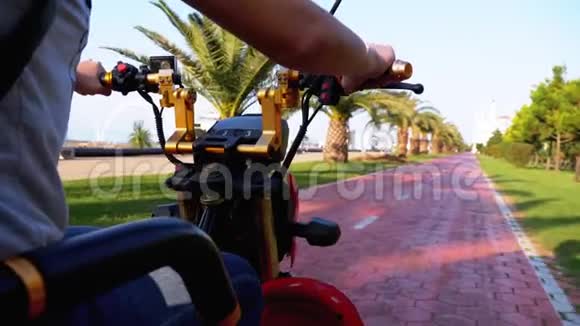 在度假小镇上女人骑着一辆电动自行车骑在一条红色的自行车小路上上面有棕榈树视频的预览图