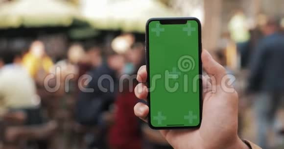 特写一个男人手拿着一部移动电话街道上有一个垂直的绿色屏幕旅游电车进入视频的预览图