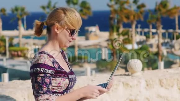 戴墨镜的游客在热带风景的背景下享受笔记本电脑视频的预览图