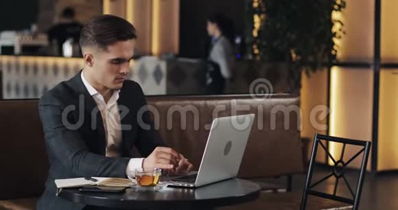 微笑的商人用笔记本电脑坐在咖啡馆的桌子旁视频的预览图