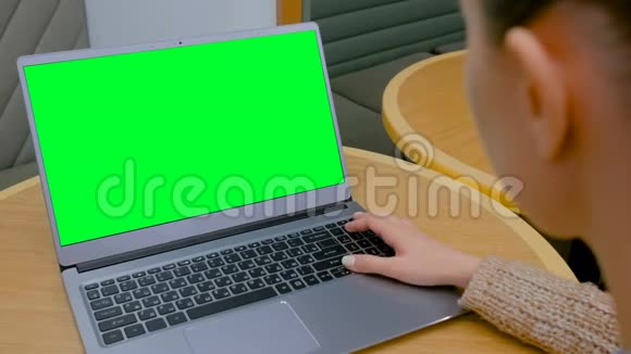 女人在咖啡馆里看着一台绿色屏幕空白的笔记本电脑视频的预览图