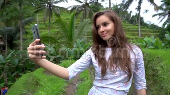 巴厘岛米台背景上的女人用手机自拍视频的预览图