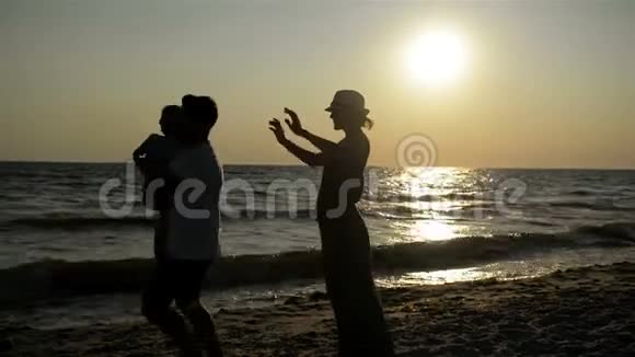 日落时分母亲和父亲与小女儿在海边的黑暗剪影肖像视频的预览图