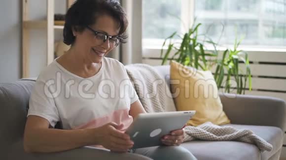戴眼镜的女人坐在舒适的家里的沙发上微笑着视频的预览图