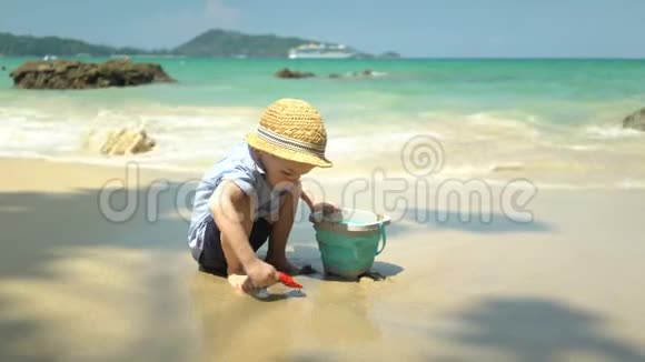 男孩在海边的海滩上玩他挖沙子扔进桶里视频的预览图