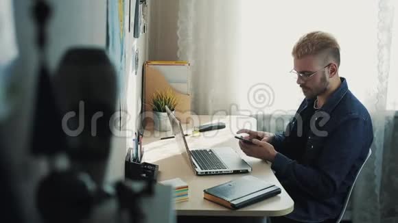 年轻有魅力的商人戴着黄色头发的眼镜在家工作坐在桌子旁的电话里说话视频的预览图