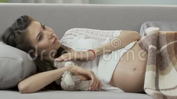 期待女性和泰迪熊躺在沙发上把手放在肚子上打盹视频的预览图