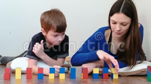用积木和立方体建造一个又小又大的塔妈妈和儿子一起玩木彩教玩具视频的预览图