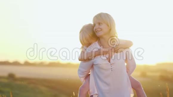 一位很酷的年轻母亲和她漂亮的女儿在草坪上玩耍享受着夏天的日落和大自然视频的预览图