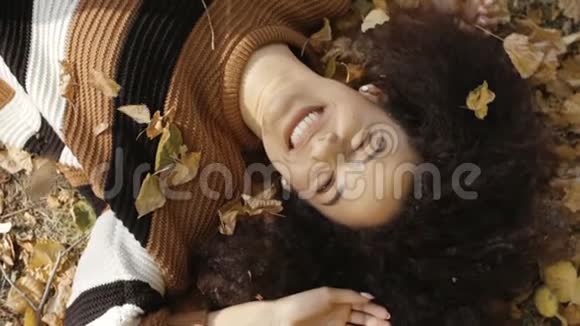 年轻的美国妇女躺在阳光明媚的公园秋叶上视频的预览图