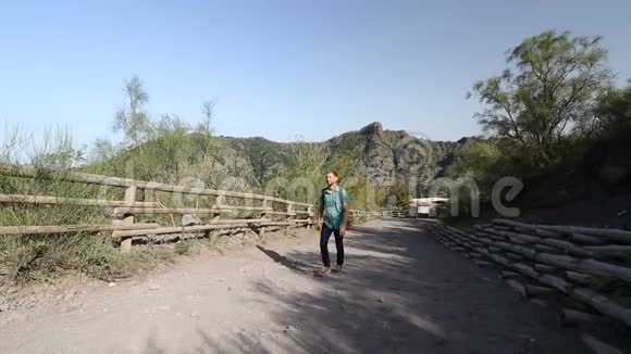 阳光明媚的一天年轻的男性背包客沿着山路上坡视频的预览图