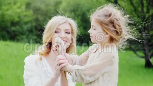 一个漂亮的金发女孩在绿色森林里和母亲一起吹蒲公英视频的预览图