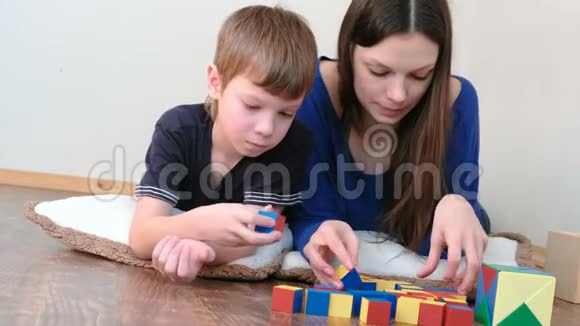 学习颜色和形状妈妈和儿子一起玩木制彩色教育玩具积木躺在地板上视频的预览图