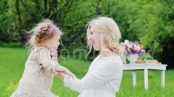 一位留着卷发的时髦年轻妈妈和她的孩子在花园里玩耍笑得很开心视频的预览图