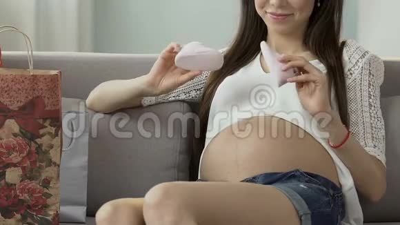 未来的母亲手里拿着婴儿鞋在肚子上轻敲期待着视频的预览图