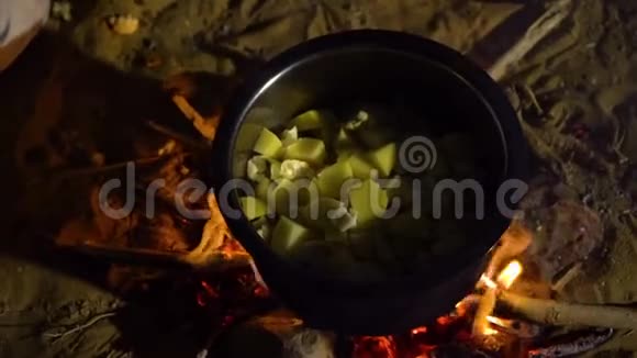 一名男子在篝火上将蔬菜倒入沸腾的锅中的近距离射击视频的预览图