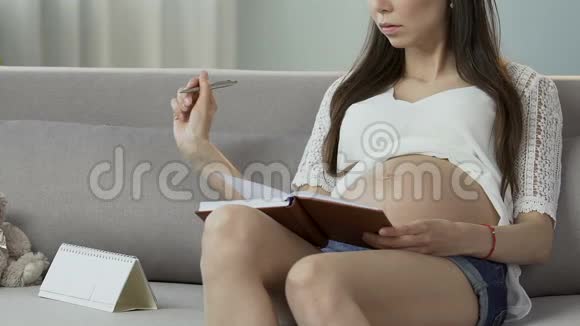 孕妇坐在笔记本和日历上计算天数怀孕数视频的预览图