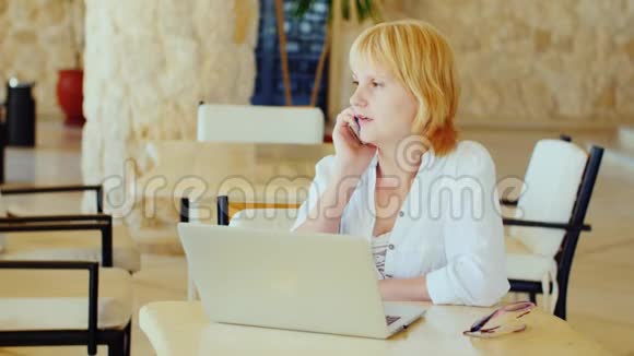 商务女性度假坐在笔记本电脑旁在电话里说话轻便的夏装视频的预览图