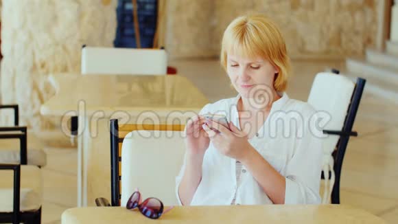 一个穿着夏装的女人正在咖啡馆里休息用电话与这个概念有关的假期视频的预览图