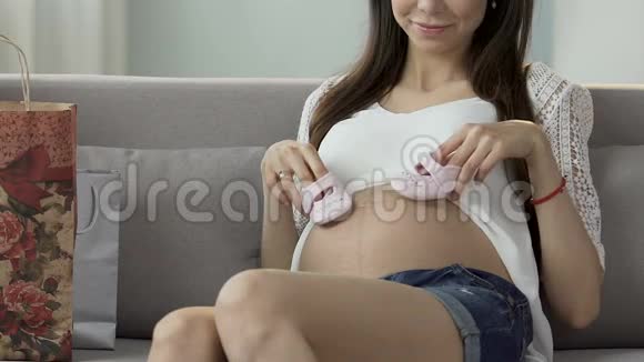 年轻的女伴拿着婴儿鞋在肚子上迈着小步幸福视频的预览图