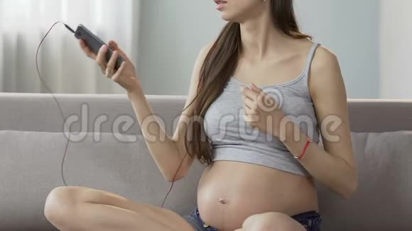 期待女人坐在沙发上从手机上选择歌曲舒缓的音乐视频的预览图