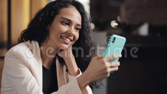 年轻商务女性在舒适的咖啡店使用手机她浏览网上留言和回复短信视频的预览图