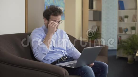 坐在沙发上戴眼镜的男人在笔记本电脑上在线购物科技视频的预览图