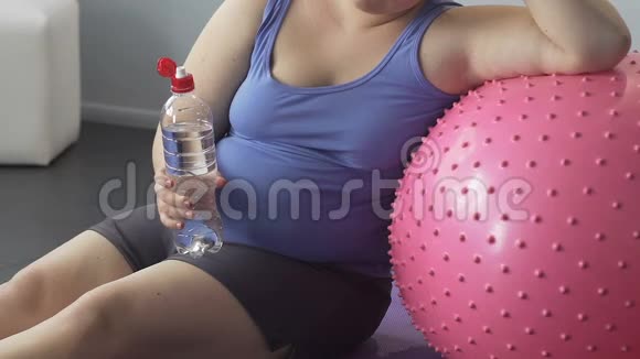 胖小姐坐在地板上喝水靠在健身球上锻炼身体视频的预览图