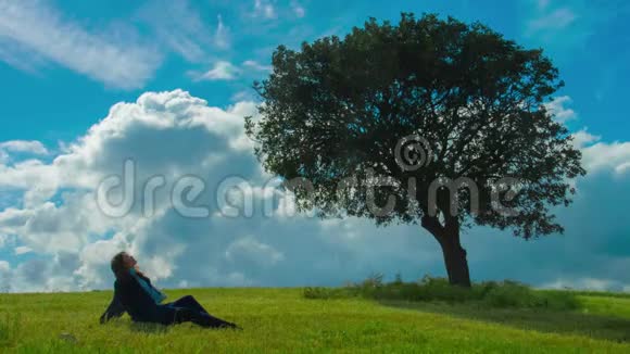 孤独的女人坐在绿树下享受着晴朗的风和日丽的天气想着视频的预览图