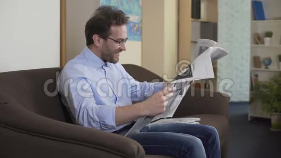 快乐的男人在报纸上看占星术享受生活周末在家视频的预览图