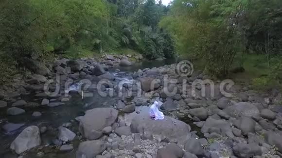 空中观景妇女在石头上祈祷飞过河流和清澈的水视频的预览图