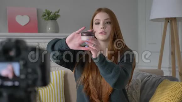 年轻的红发女孩博客作者微笑着对着镜头说话展示了一种新的购买化妆品胭脂腮红粉末视频的预览图