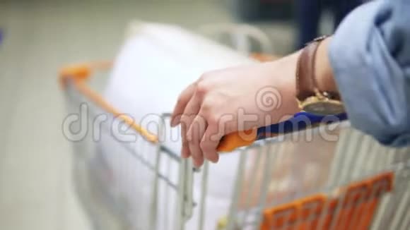 在超市里一个女人的手拿着一辆手推车推着一辆手推车背面视图视频的预览图